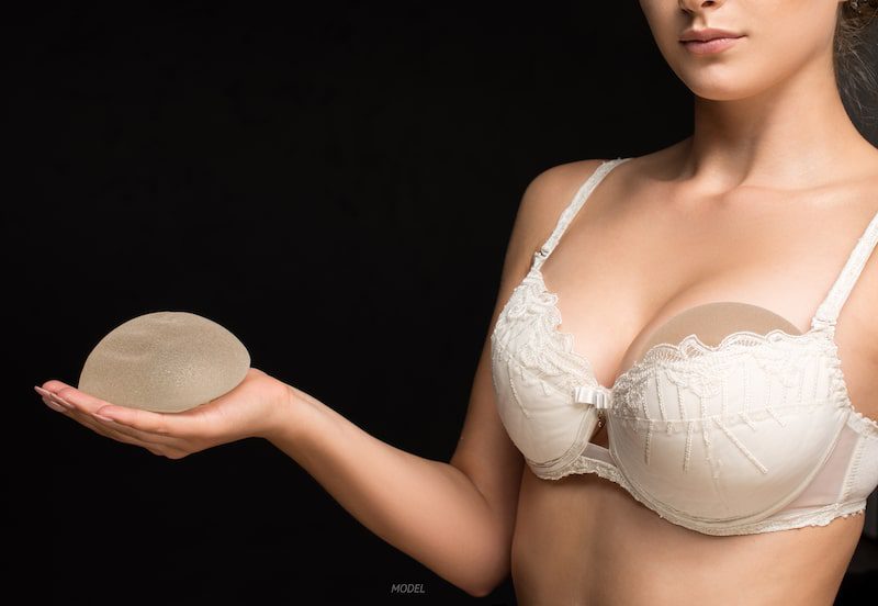 Women with natural breast and implant in hand